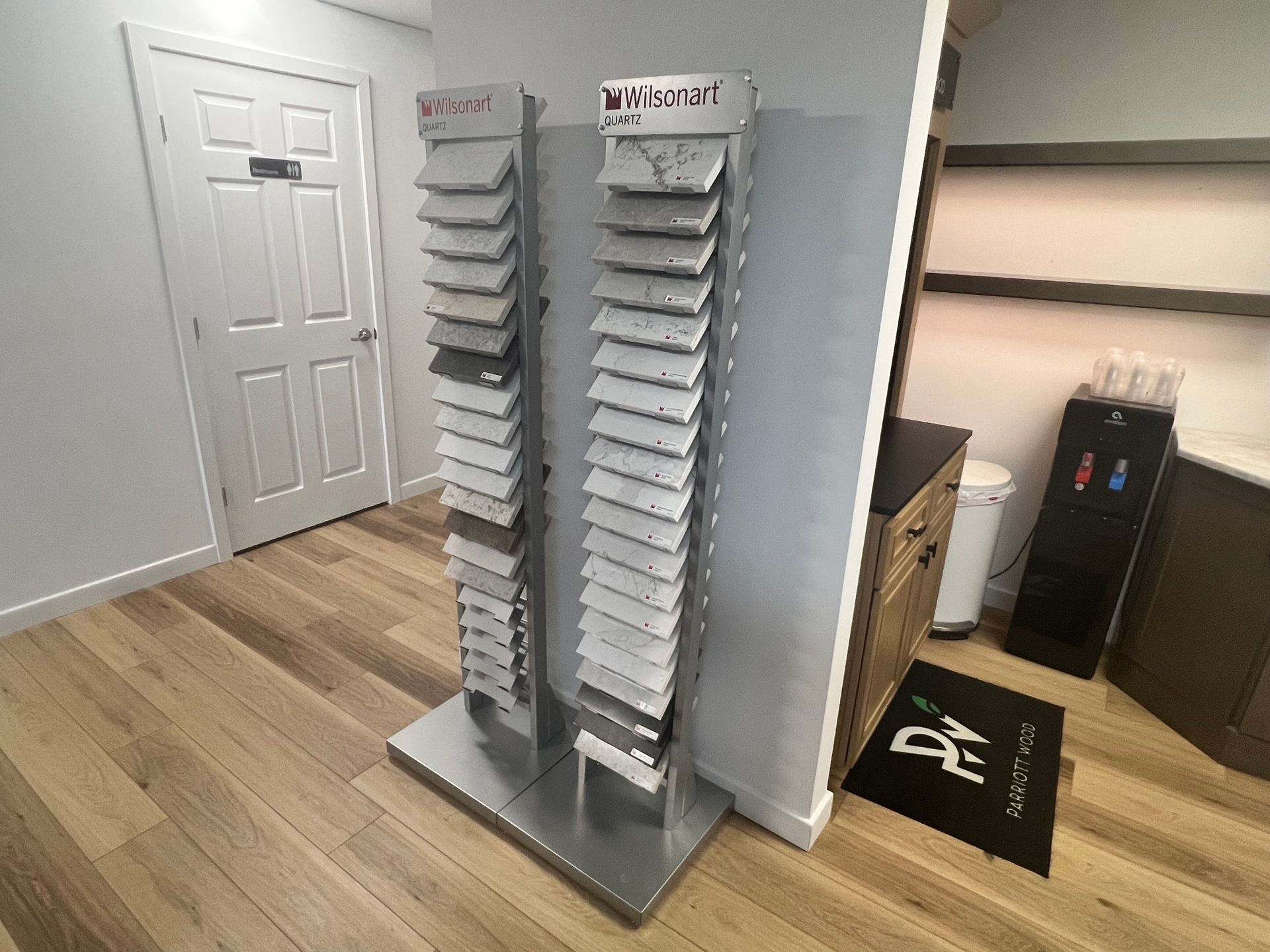 Sample tile displays stand in a showroom, with a white door and wood flooring.