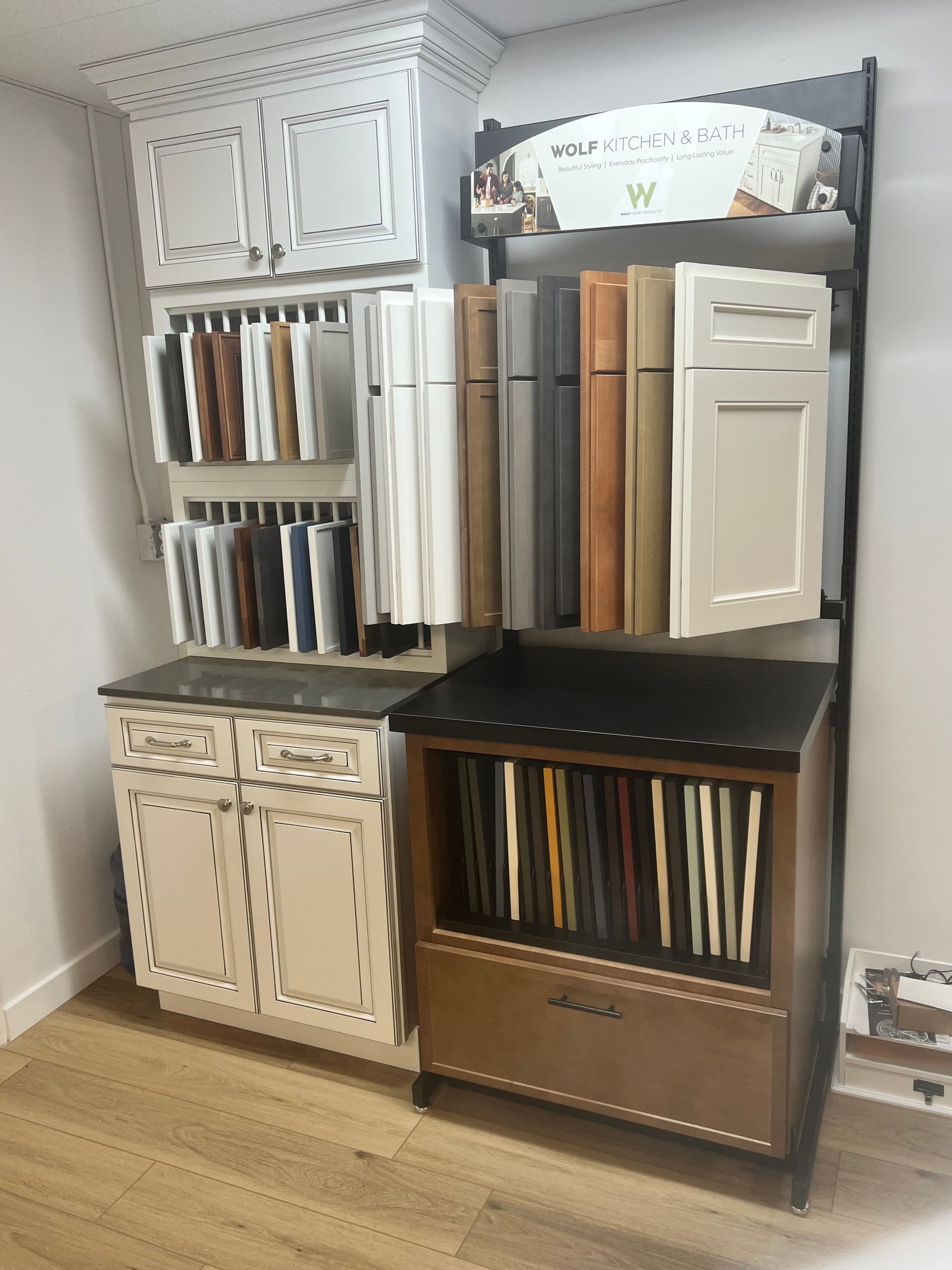 Cabinetry display with wood and painted door samples, countertops, and brochures in a showroom.