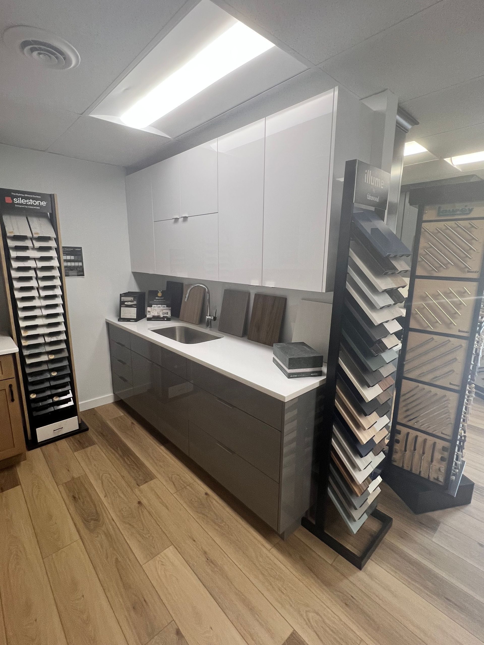 Kitchen showroom featuring cabinets, countertops, and flooring samples with wood grain floors.