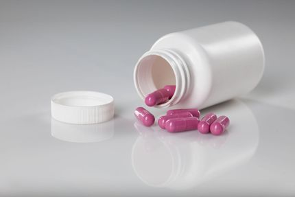 White pill bottle tipped over, spilling pink capsules onto a reflective surface.
