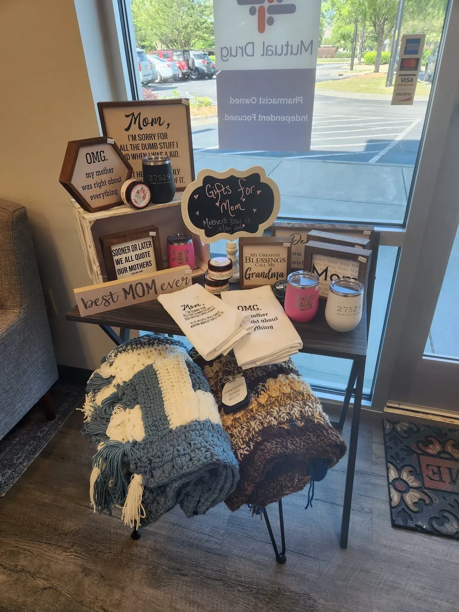 Table display of gifts: blankets, mugs, signs with Mom and decorative items.