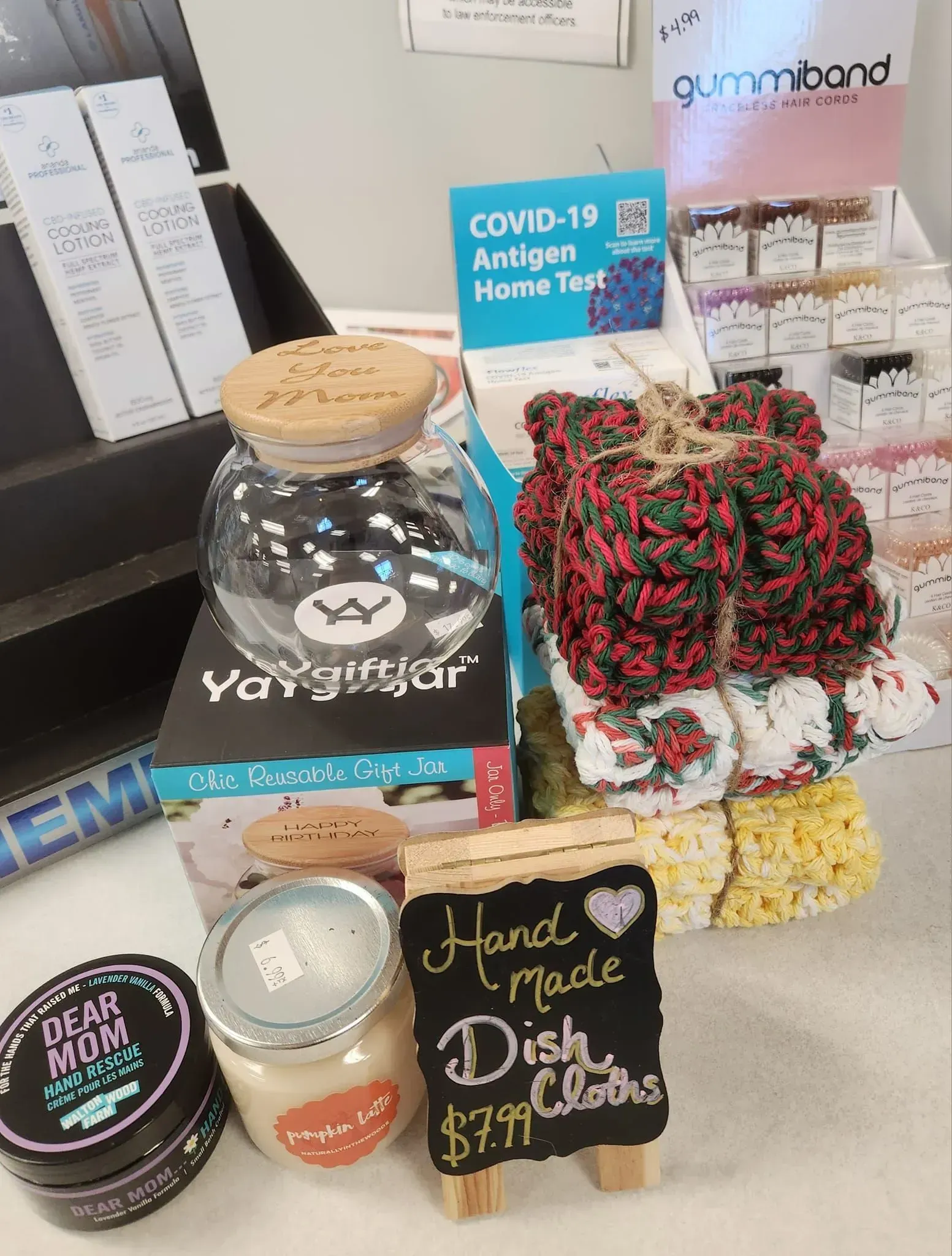 Display of handmade items: dish cloths, candles, jar of candy, and a COVID-19 test kit.