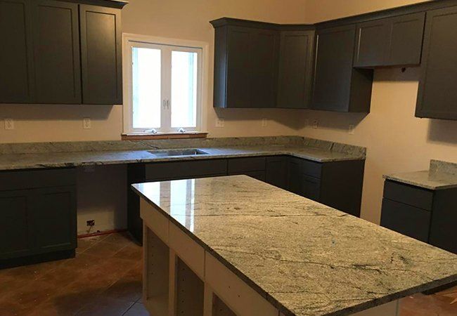 A kitchen with gray cabinets , granite counter tops , and a large island.