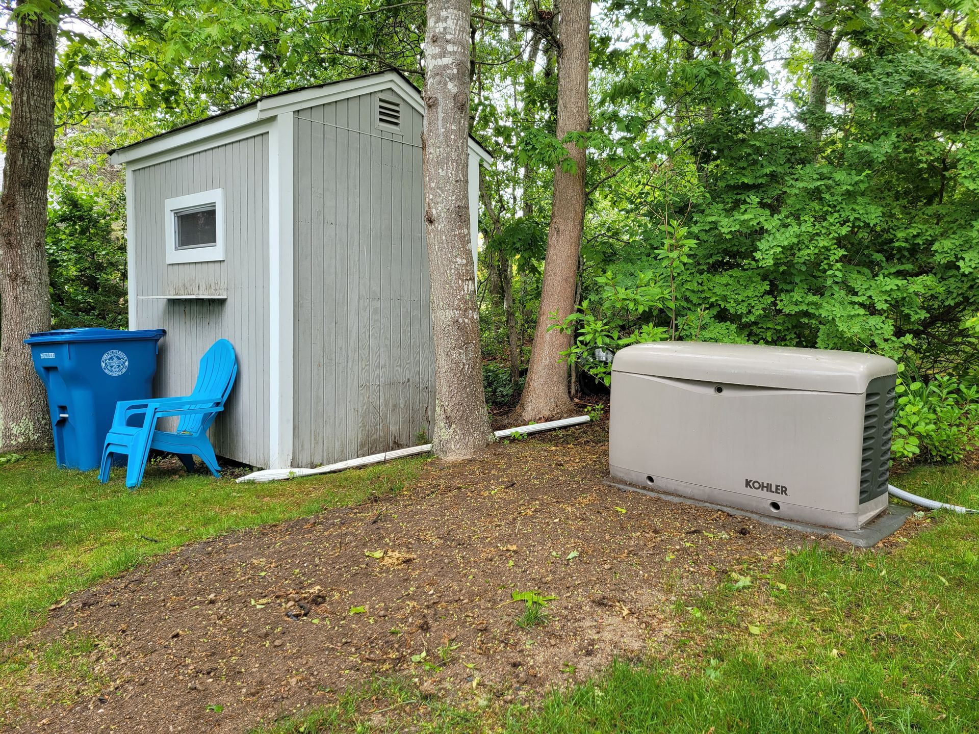 A shed with a blue chair and a generator in the backyard.