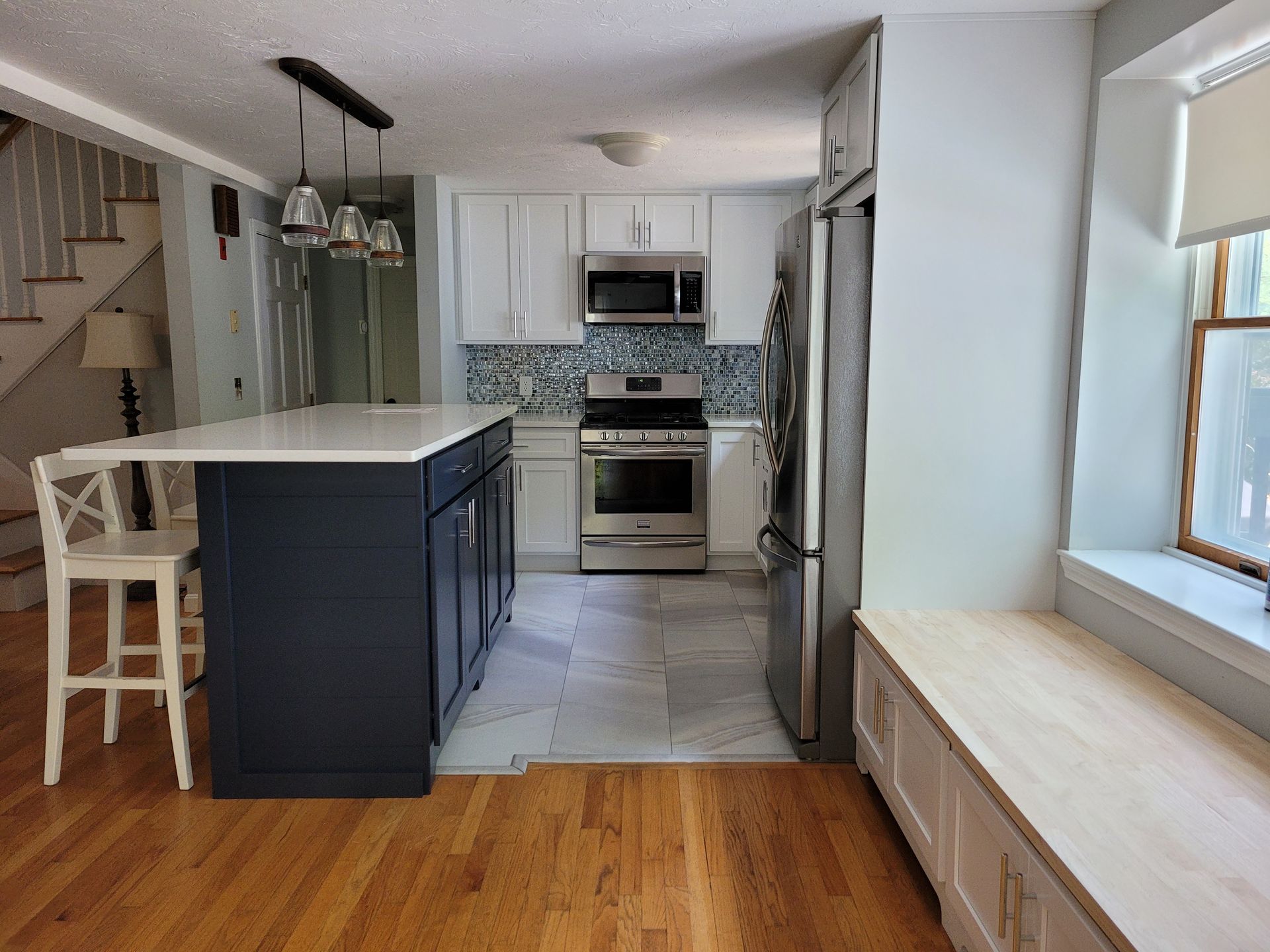 A kitchen with white cabinets , stainless steel appliances , a large island and a window seat.