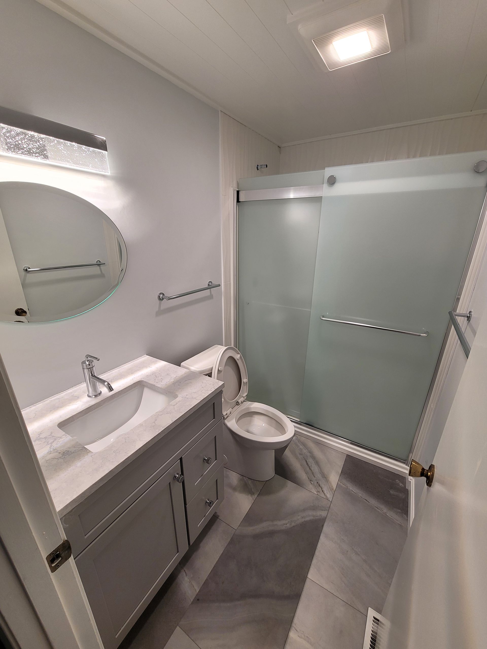 A bathroom with a toilet , sink , mirror and shower.