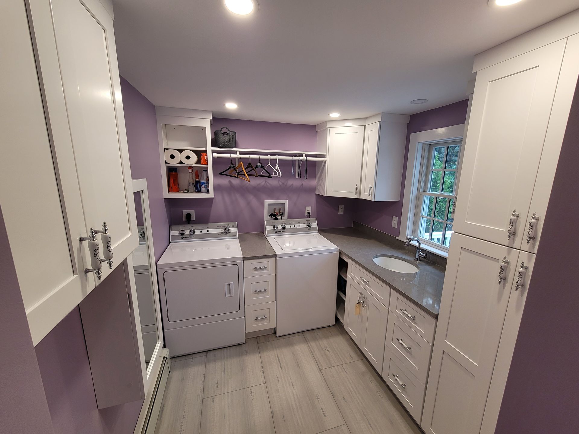 A laundry room with purple walls and white cabinets