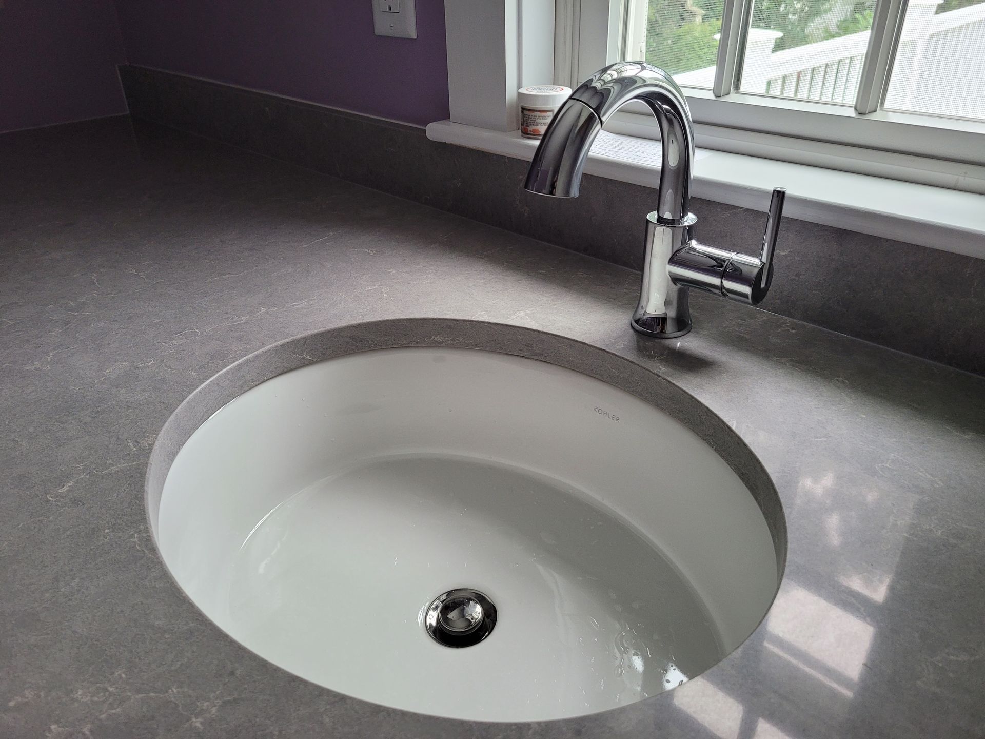 A white sink with a chrome faucet on a counter next to a window.