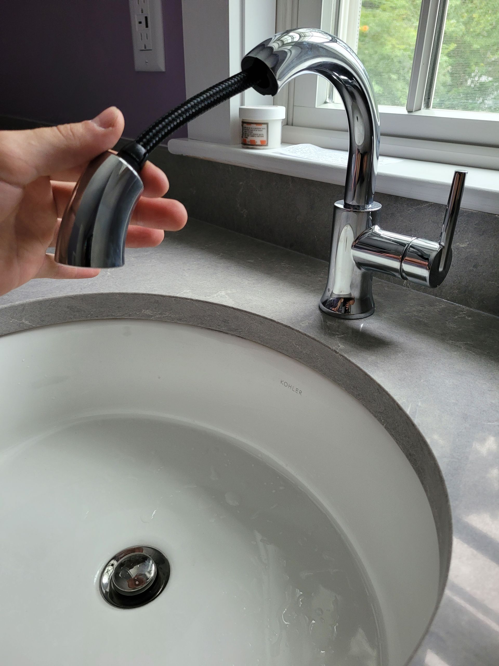 A person is holding a faucet over a sink.