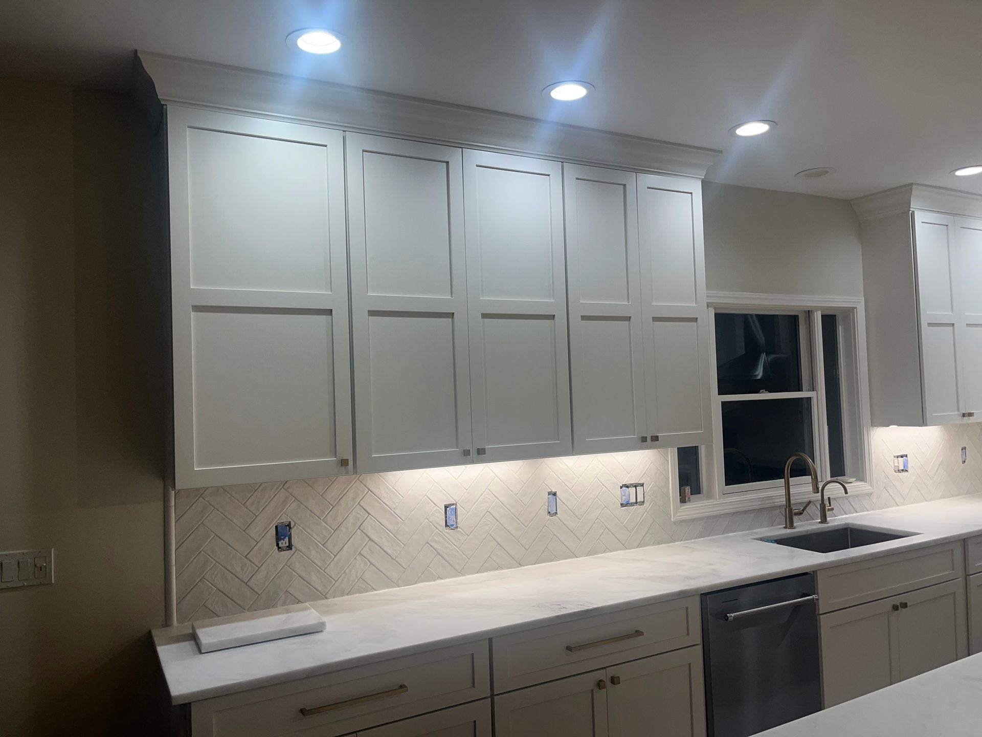 A kitchen with white cabinets , a sink , and a window.