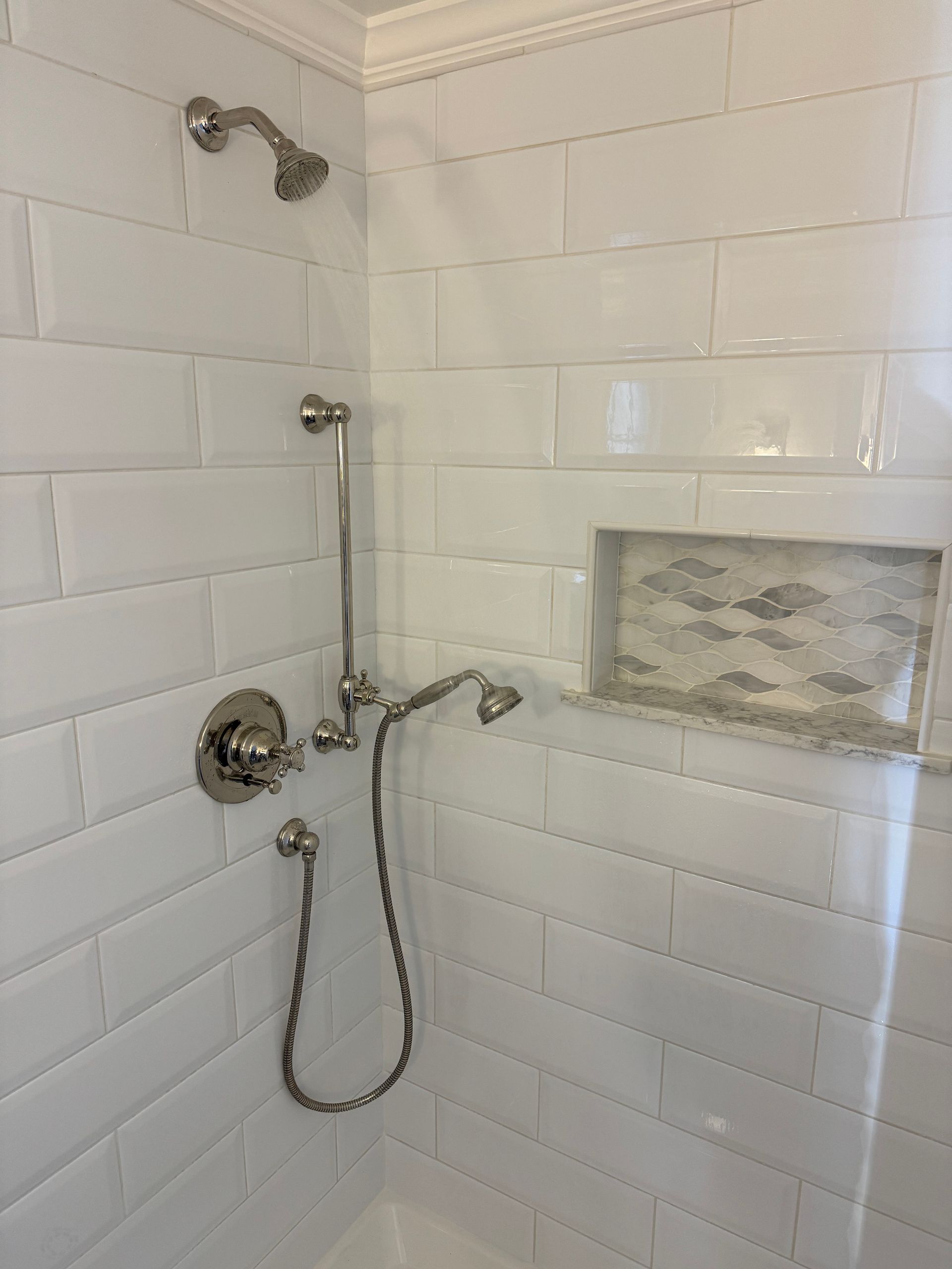 A bathroom with white tiles and a shower head.