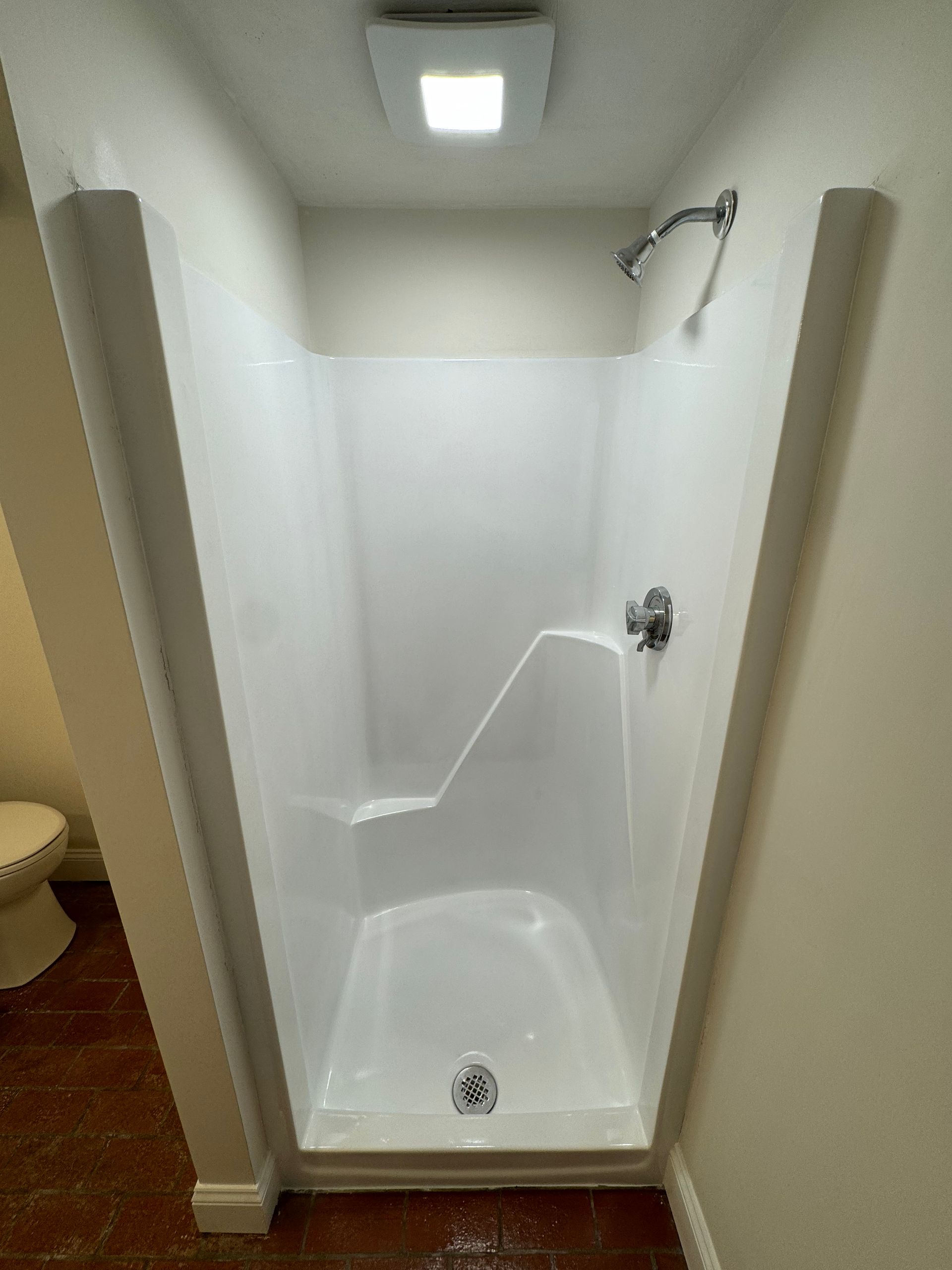 A white shower stall in a bathroom next to a toilet.