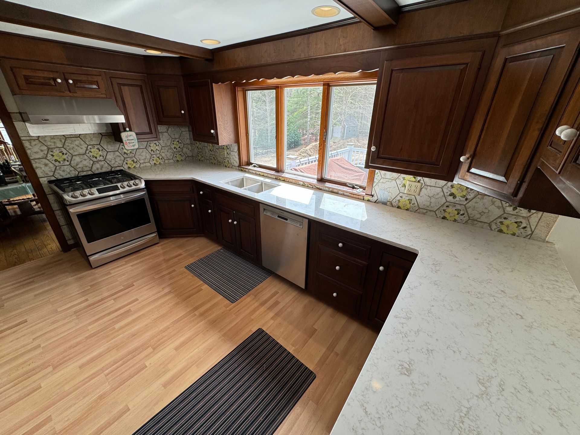 A kitchen with wooden cabinets , a stove , a sink , and a window.