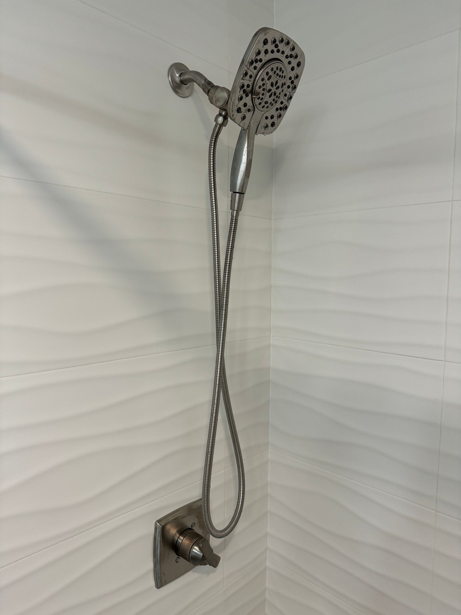 A shower head with a hose attached to it is hanging on a white wall.
