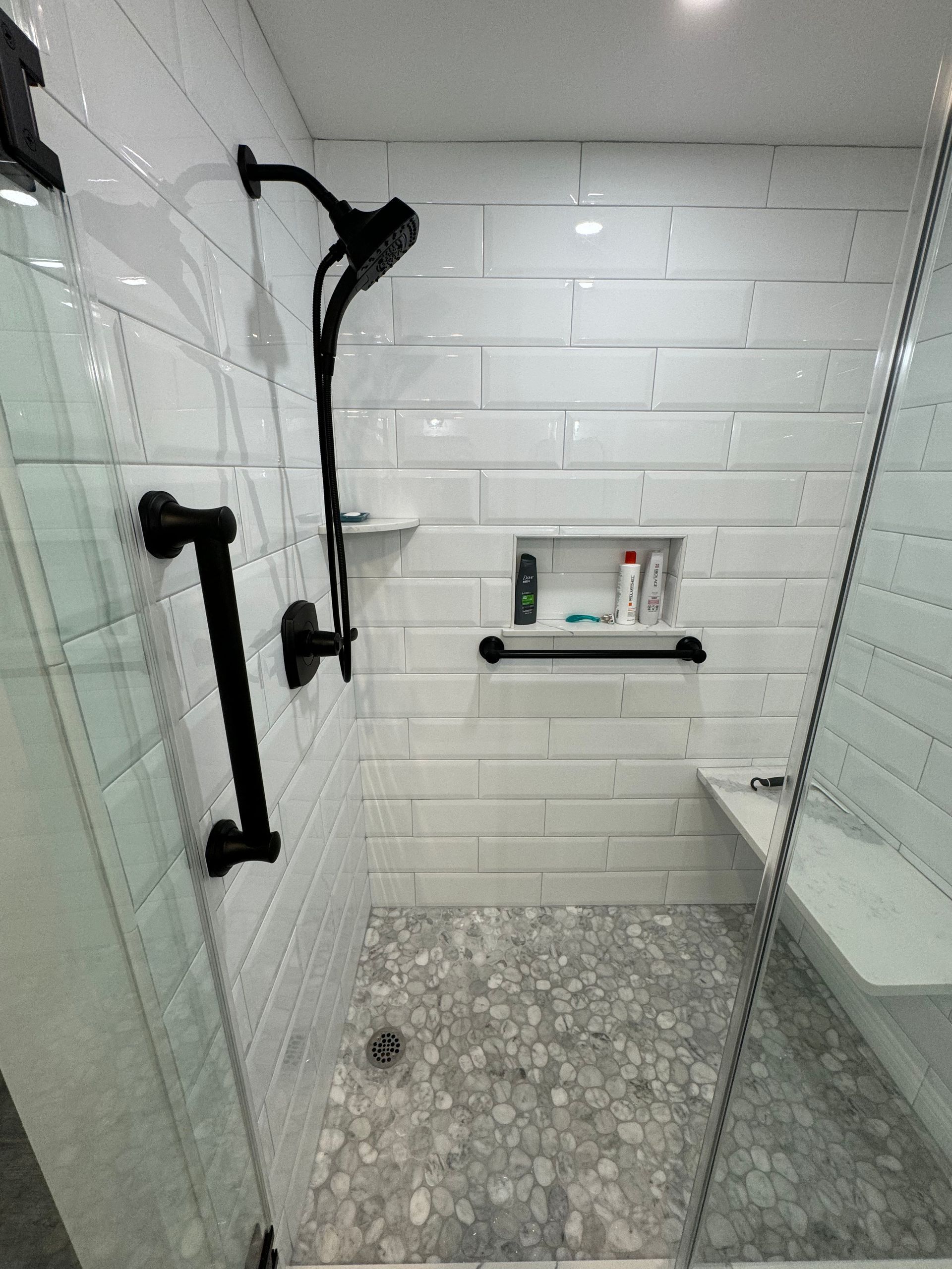 A bathroom with white tiles and a walk in shower with a bench.