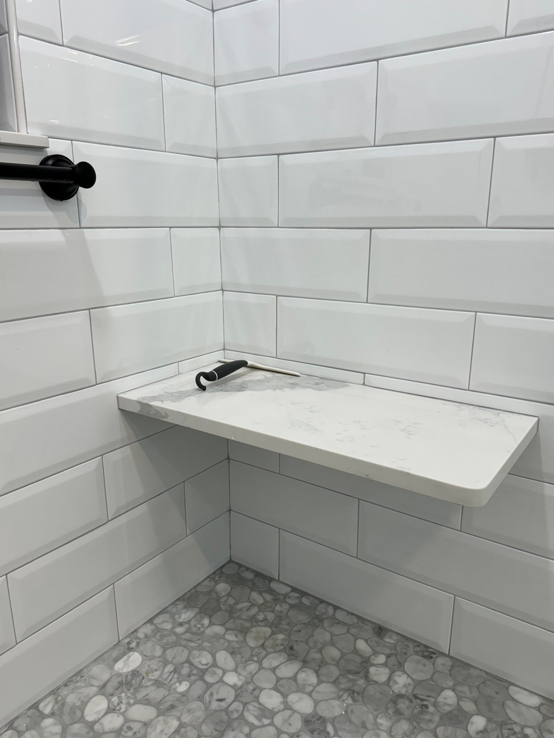 A bathroom with white tiles and a shelf in the corner.