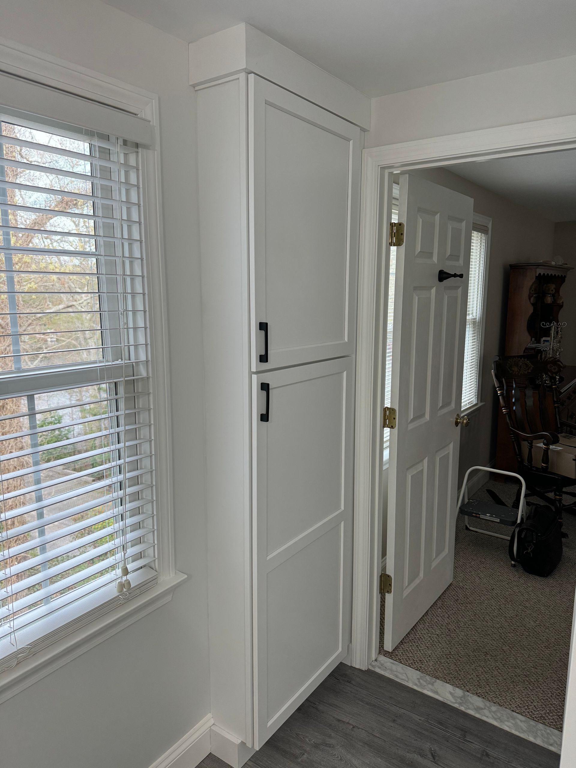 A white cabinet is sitting next to a window in a room.