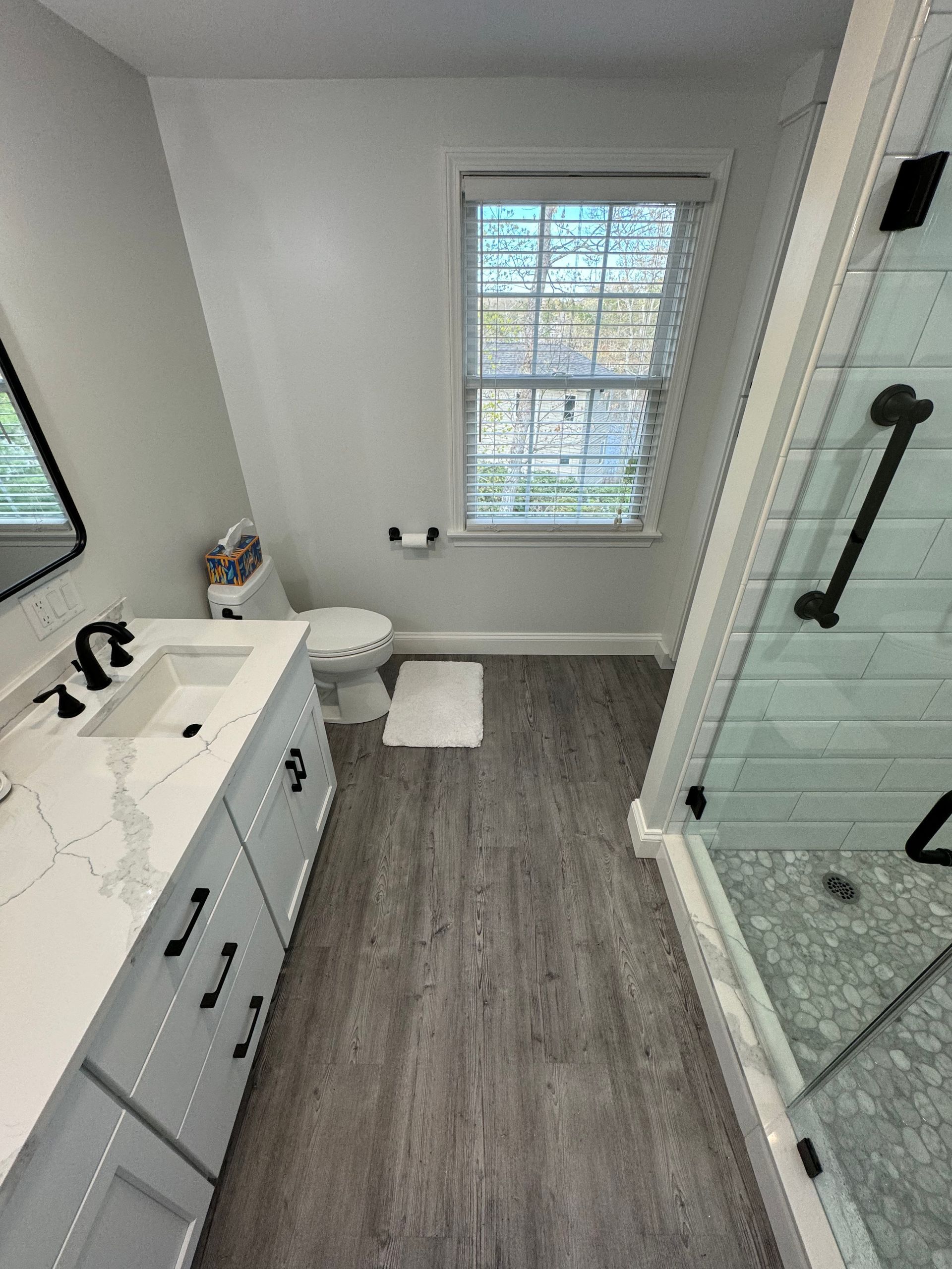 A bathroom with a sink , toilet , shower and window.