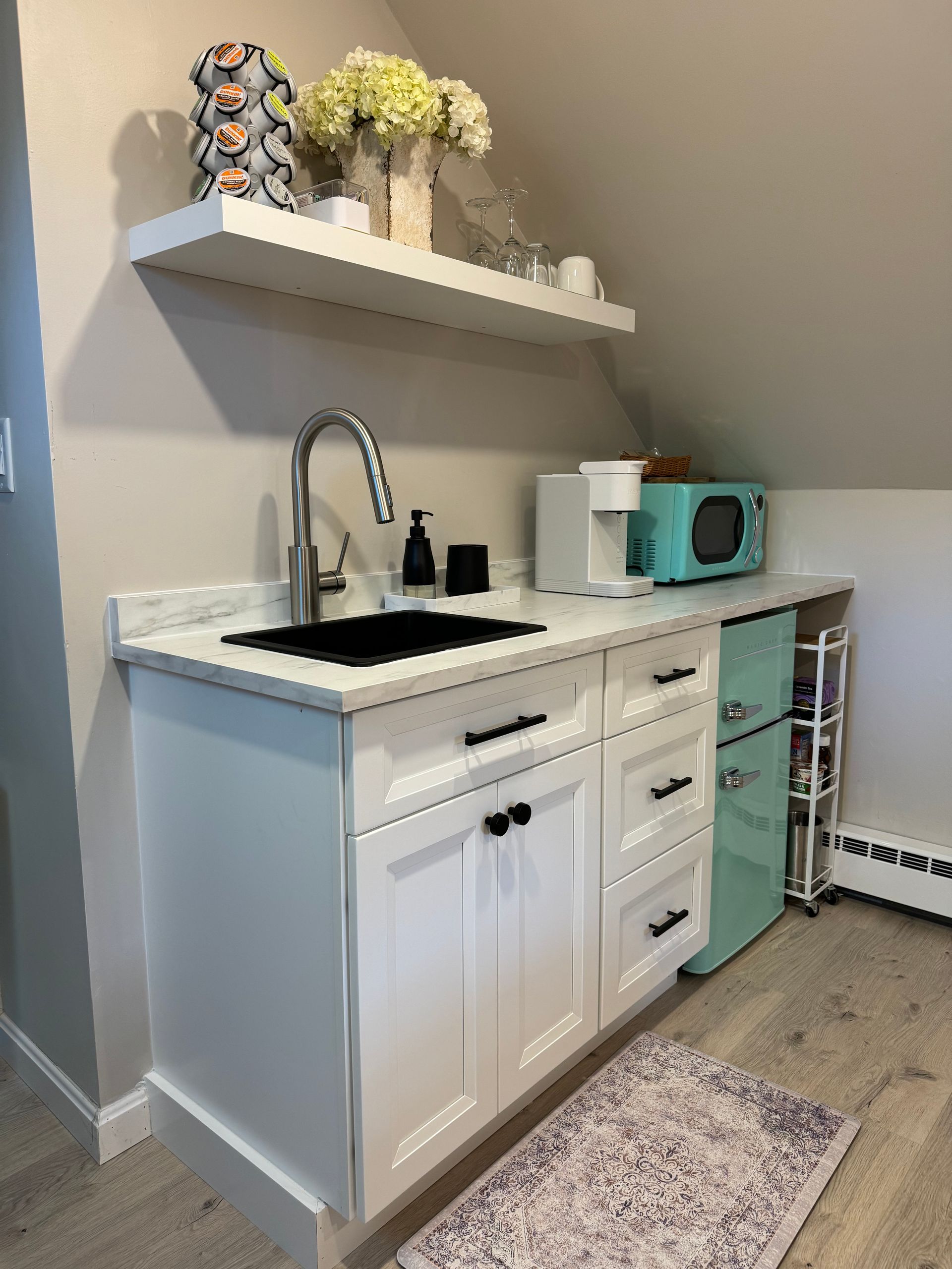 A kitchen with white cabinets , a sink , a microwave , and a rug.