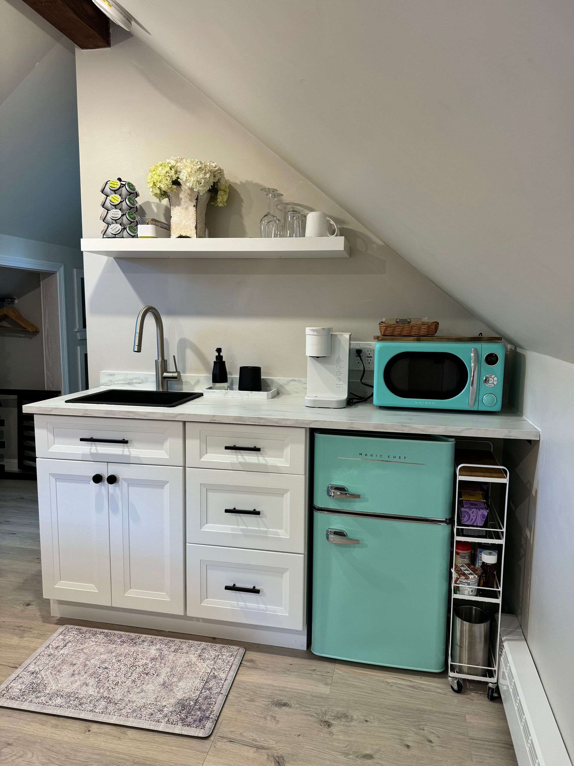 A kitchen with a sink , refrigerator , microwave and a rug.