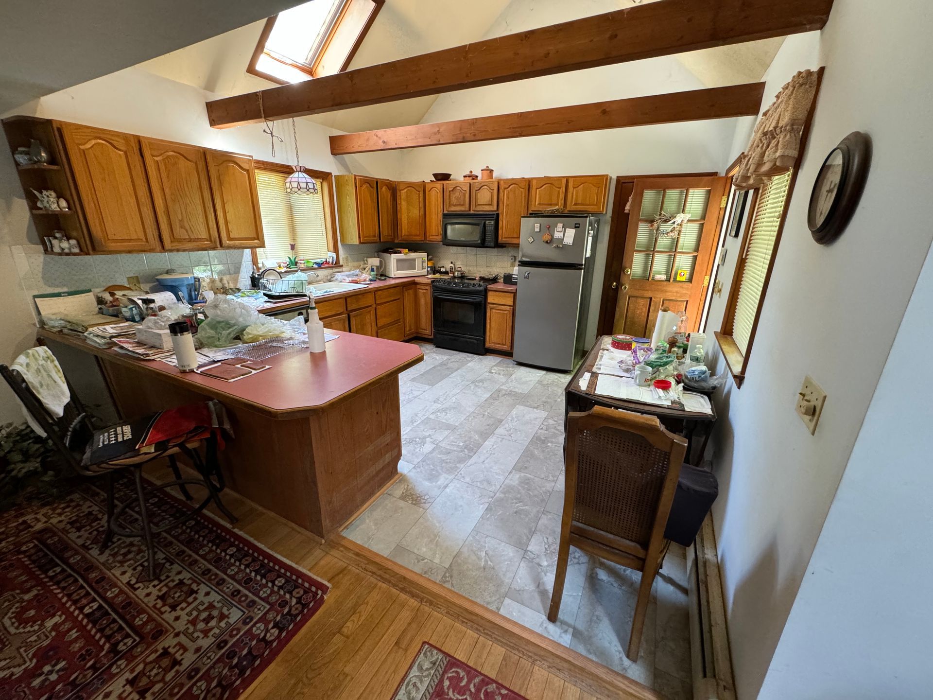 A kitchen with wooden cabinets , a refrigerator , a stove , and a clock on the wall.