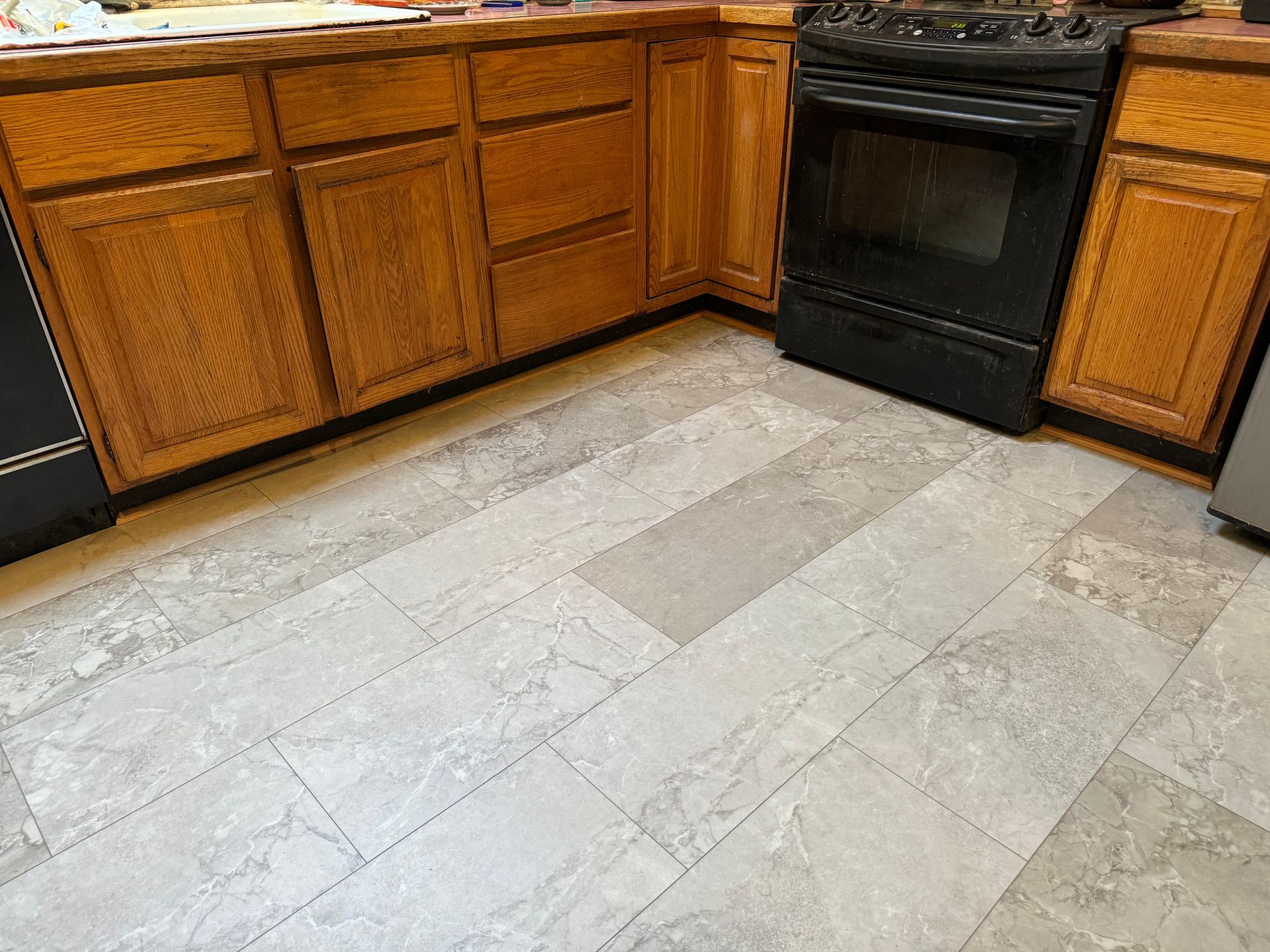 A kitchen with wooden cabinets , a stove , and a tile floor.