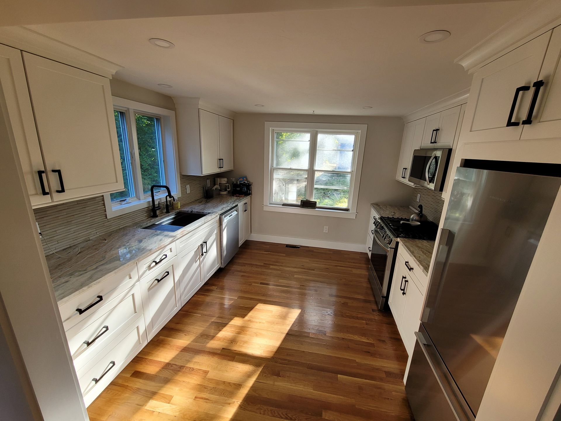 A kitchen with white cabinets , stainless steel appliances , hardwood floors and a window.
