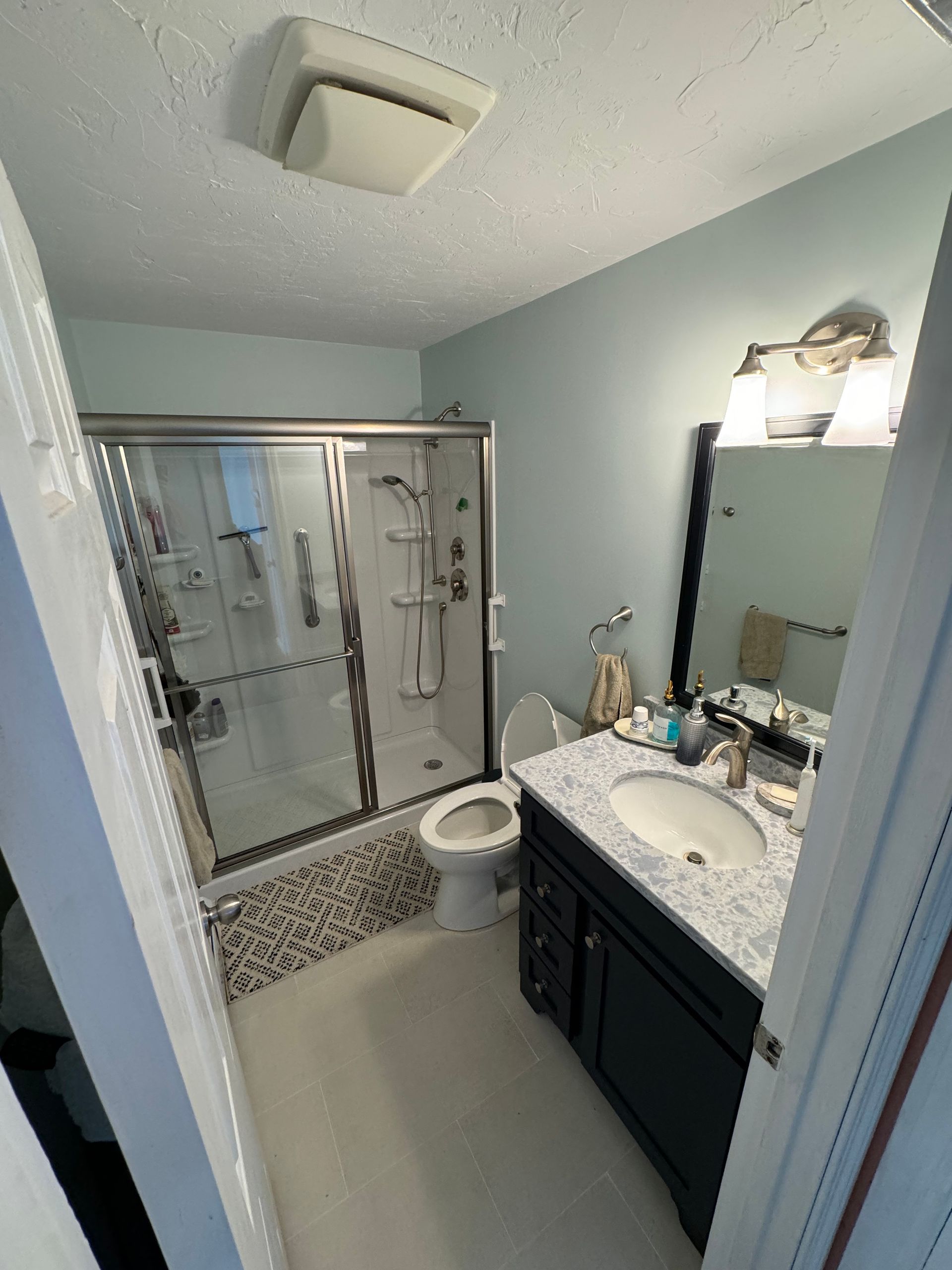 A bathroom with a toilet , sink , shower and mirror.