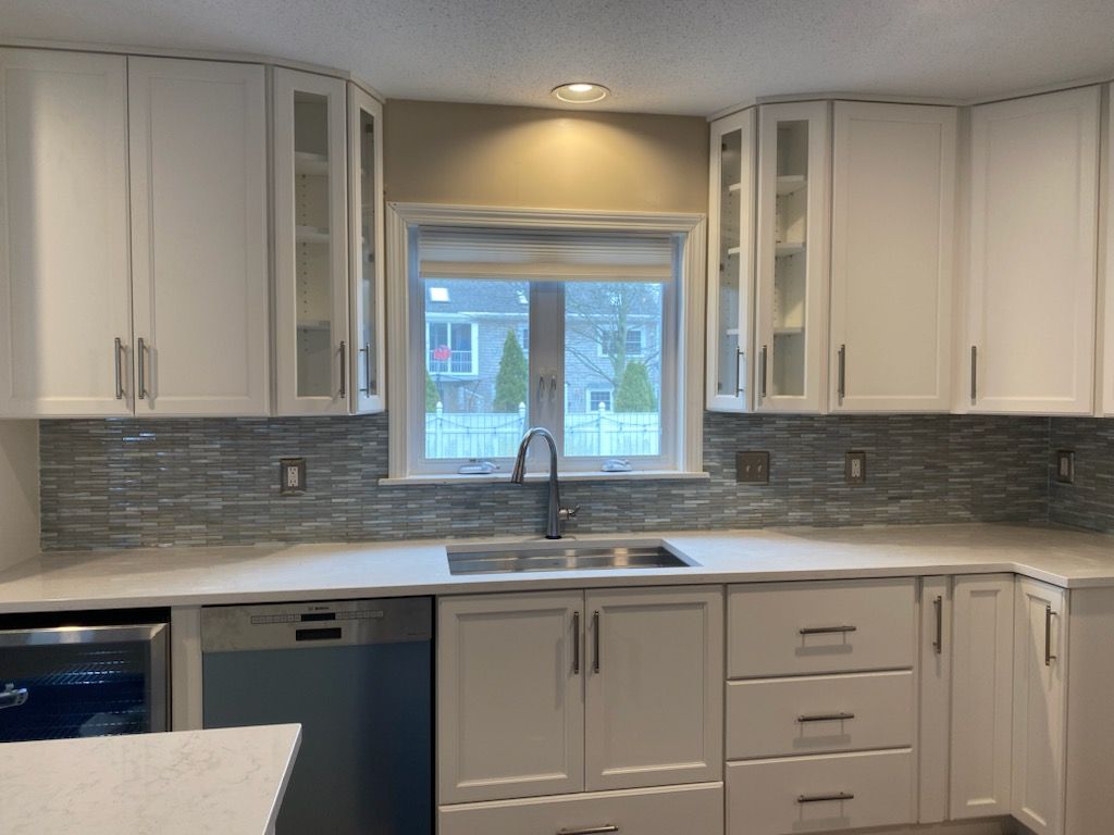 A kitchen with white cabinets , a sink , a dishwasher and a window.