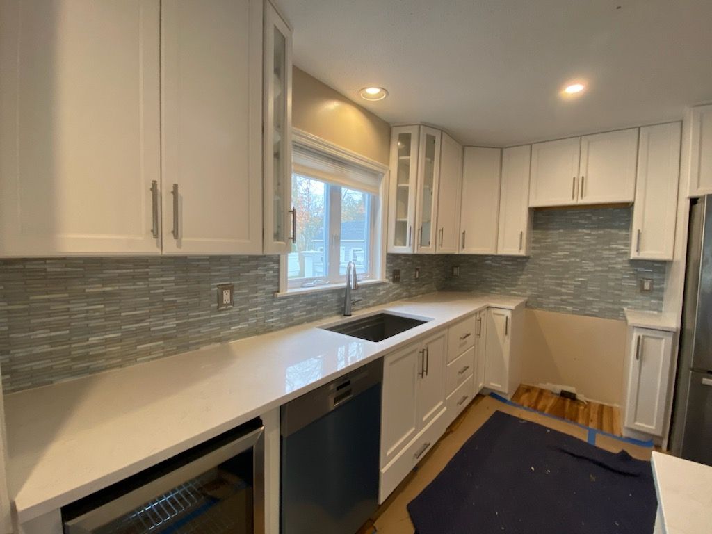 A kitchen with white cabinets , a sink , a dishwasher , and a window.