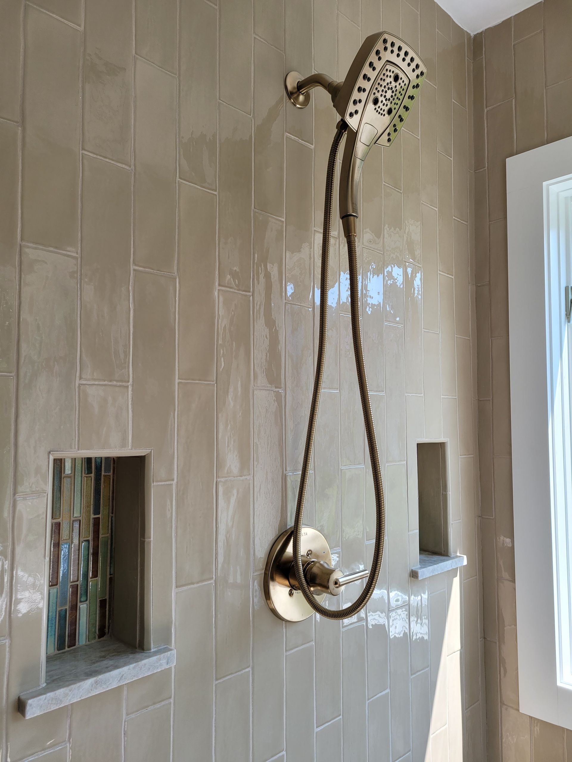 A shower head is hanging from the wall in a bathroom next to a window.