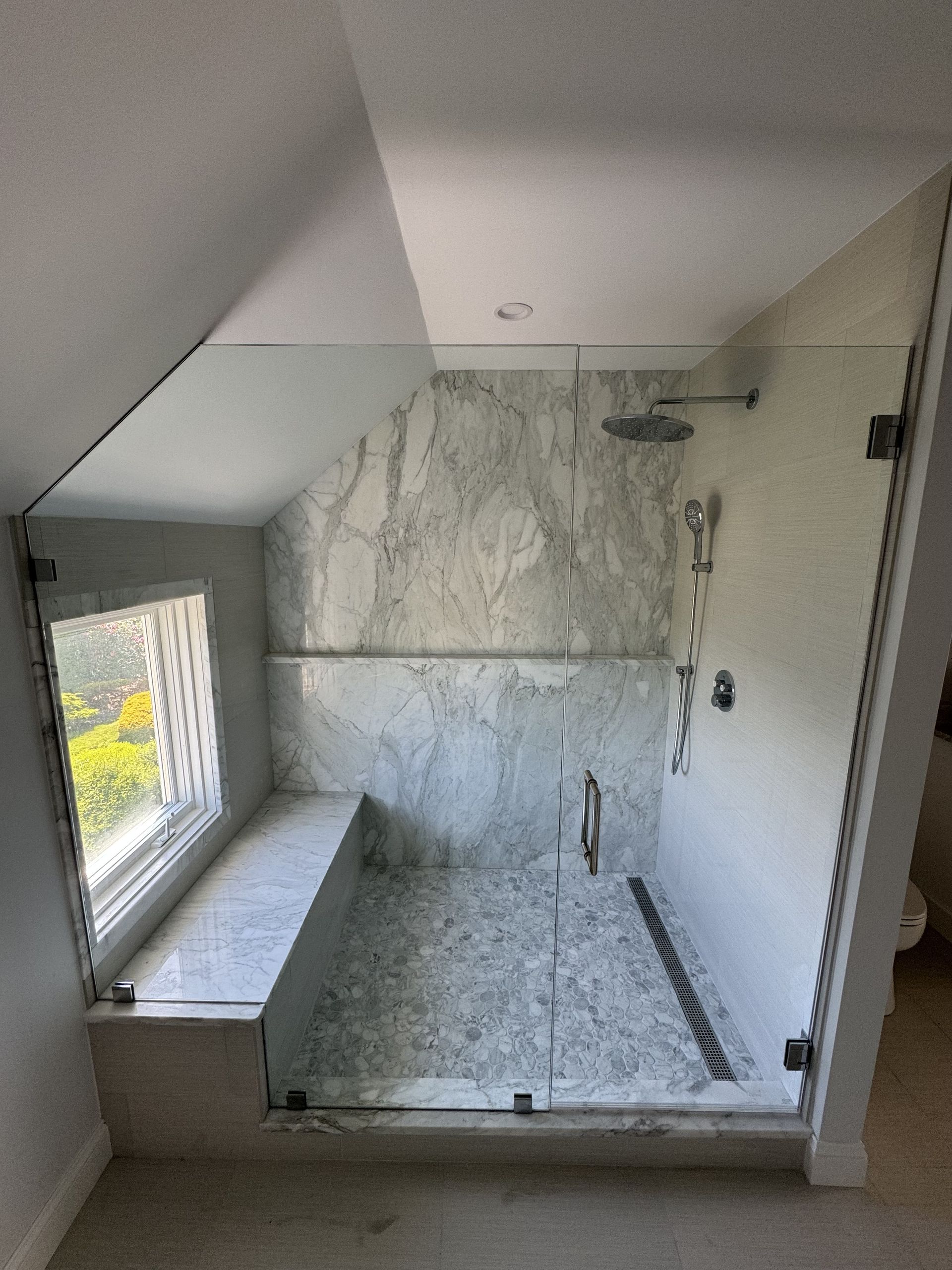 A bathroom with a walk in shower with a bench and a window.