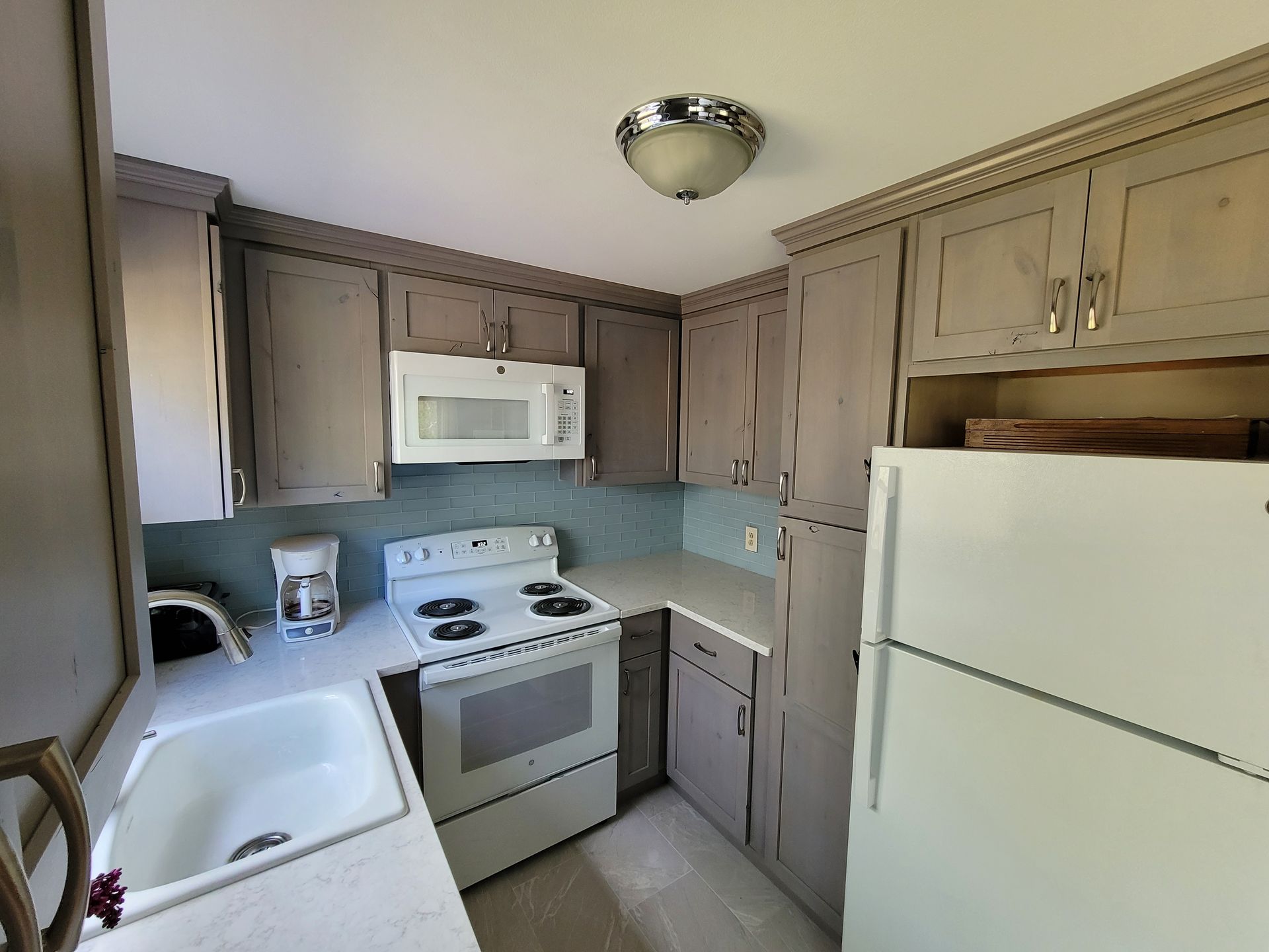 A kitchen with a stove , microwave , sink and refrigerator.