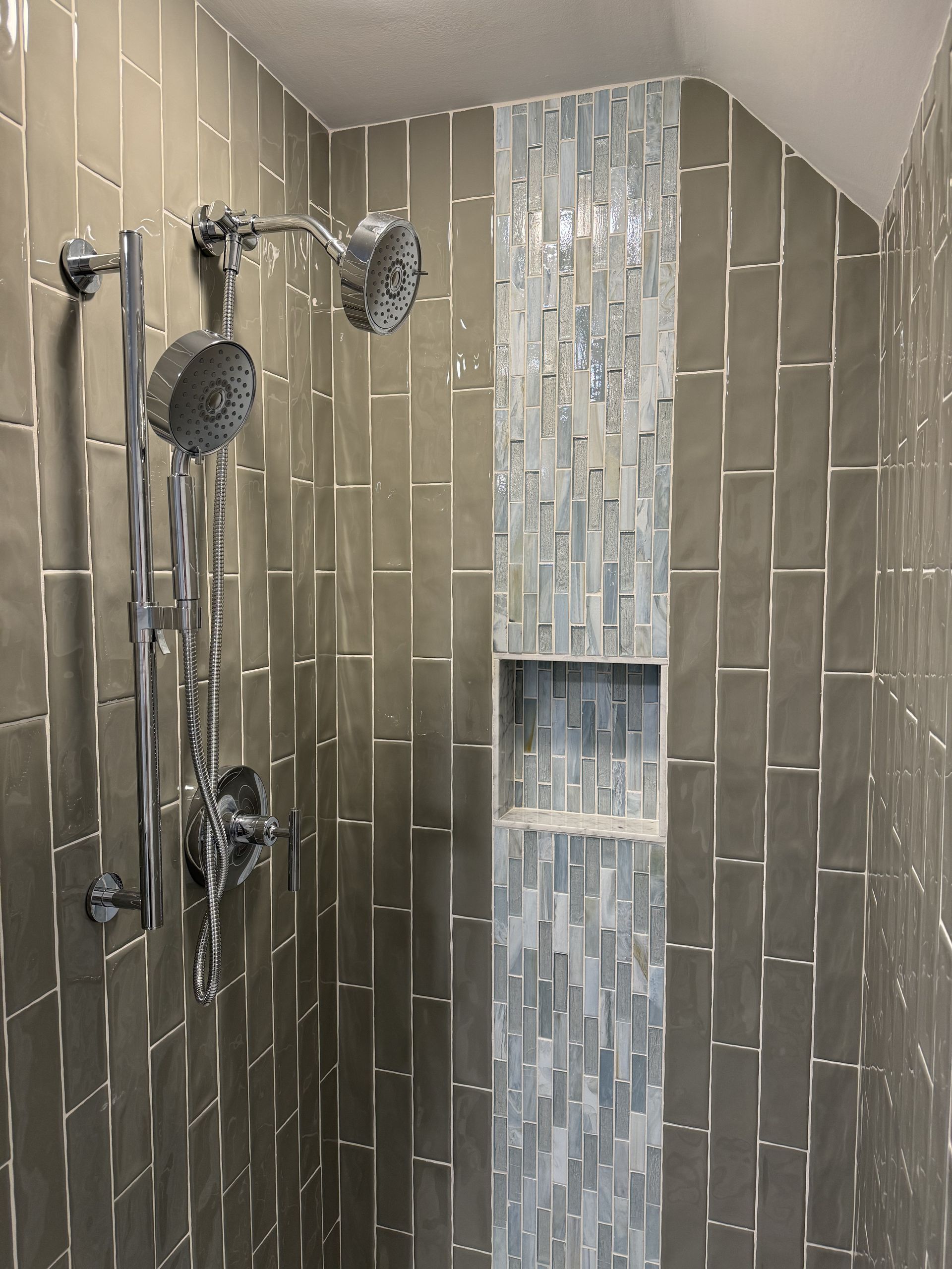 A shower with two shower heads and a shelf in the corner.