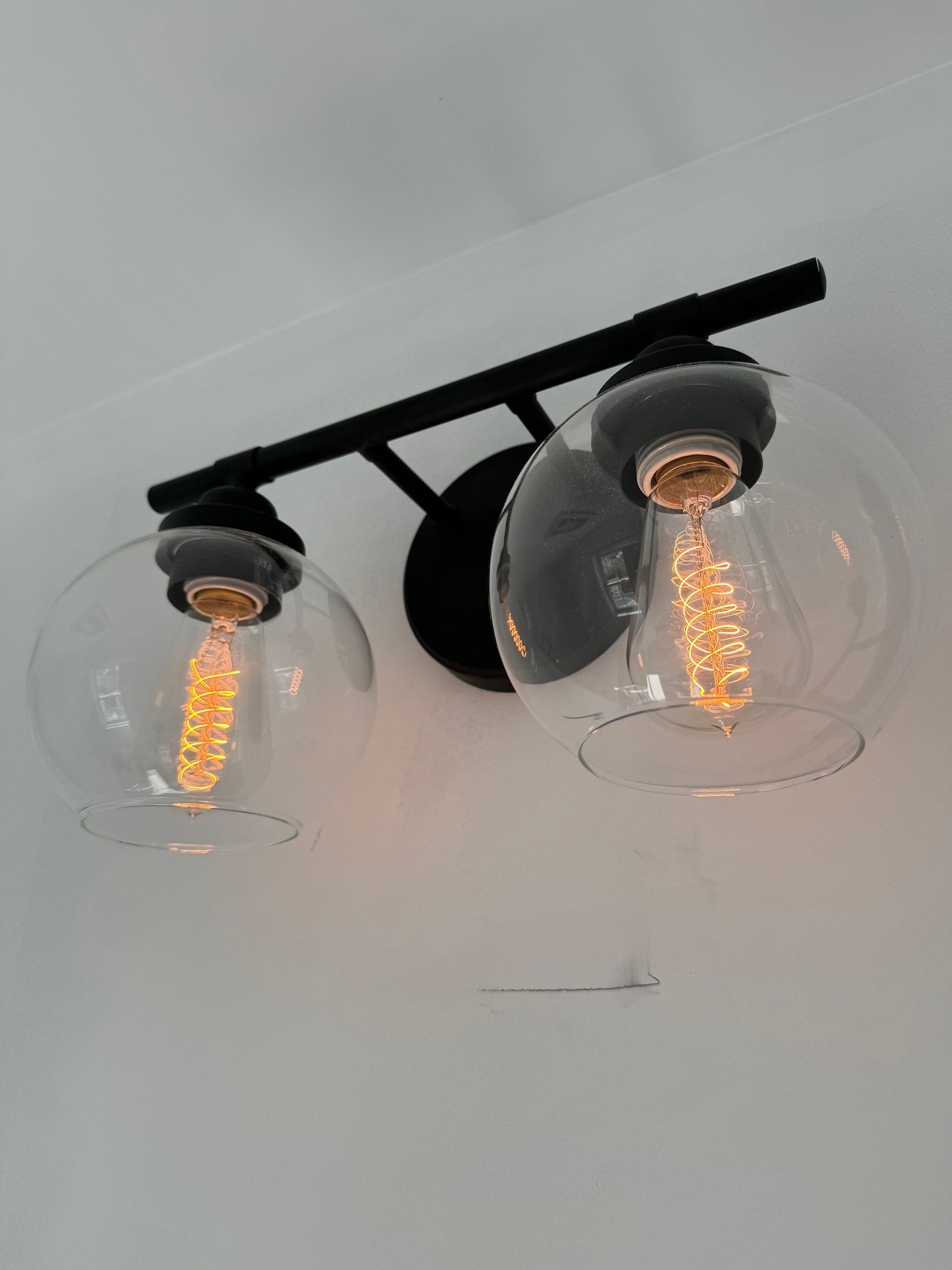 A bathroom vanity light with two clear glass shades and two light bulbs.