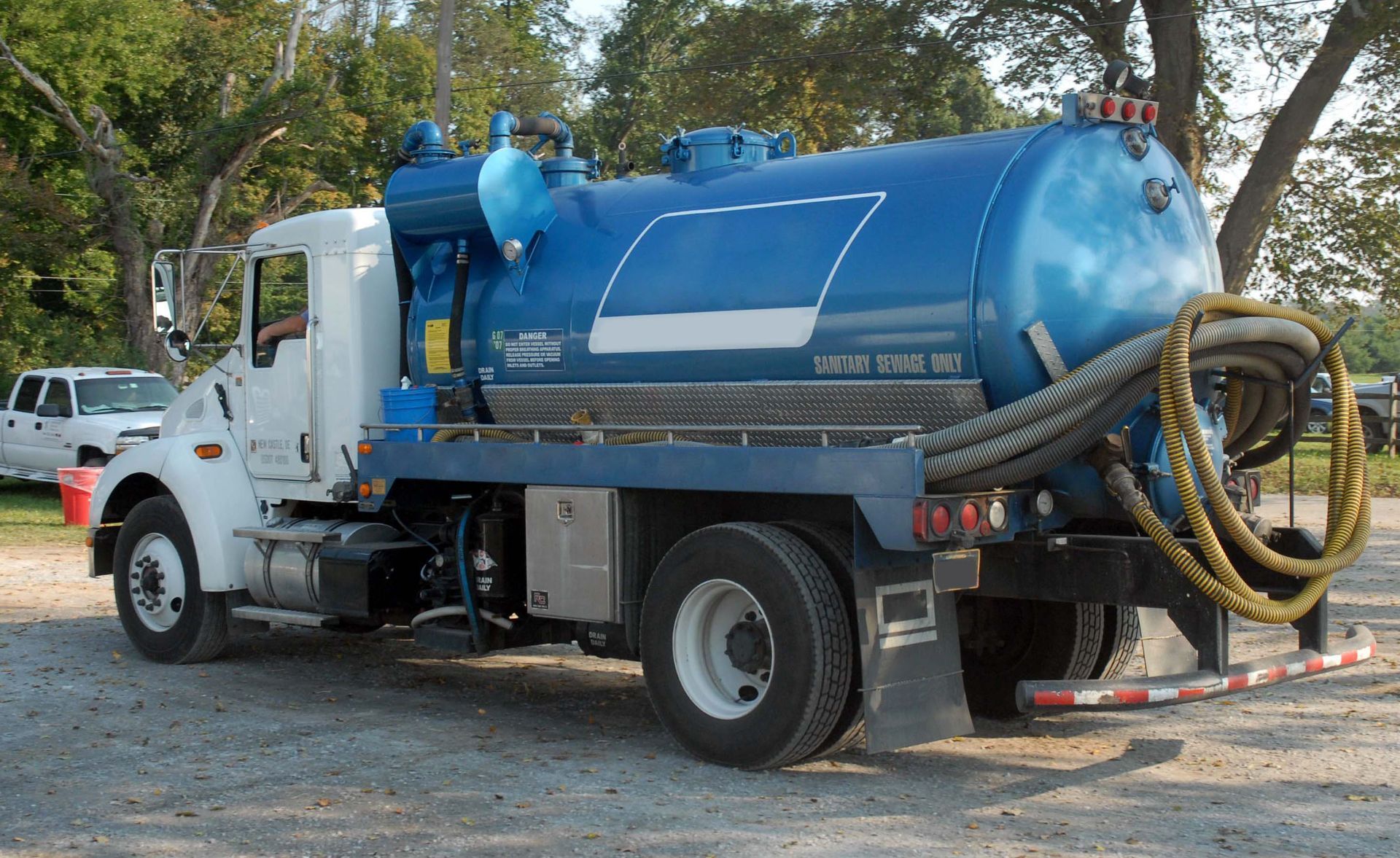 Blue and white septic tank truck parked on gravel.