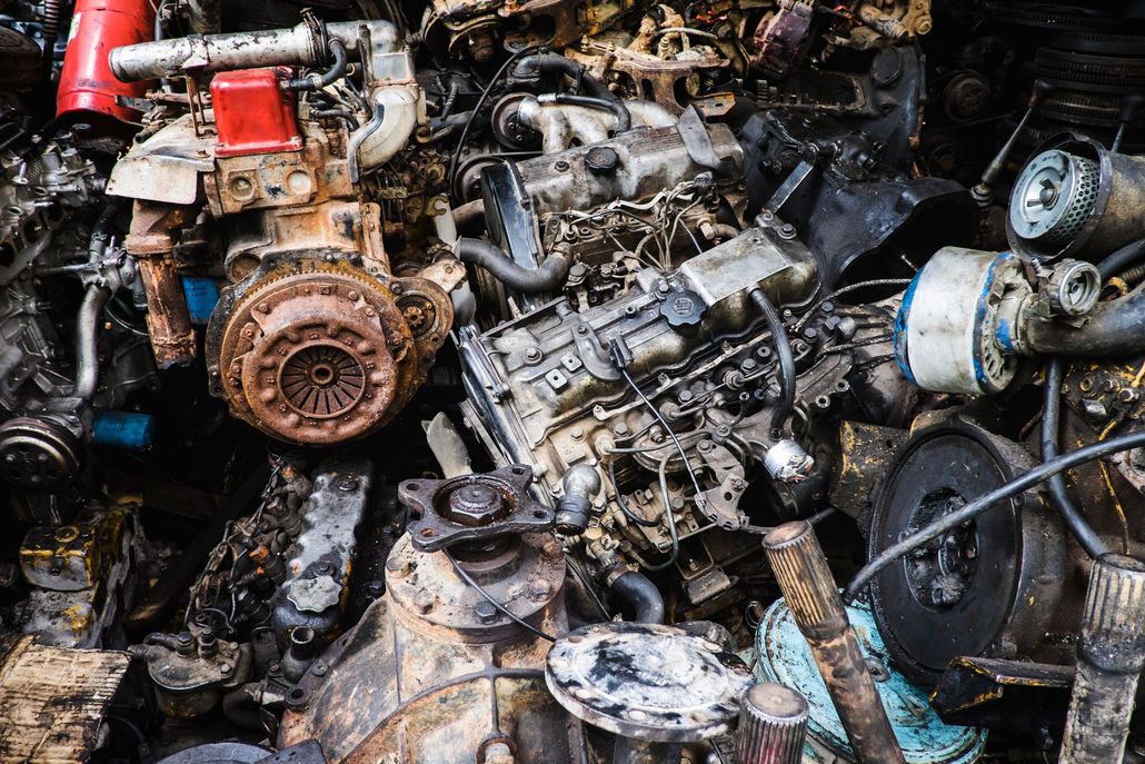 A cluttered pile of weathered, discarded automotive engines and mechanical parts in a salvage yard.