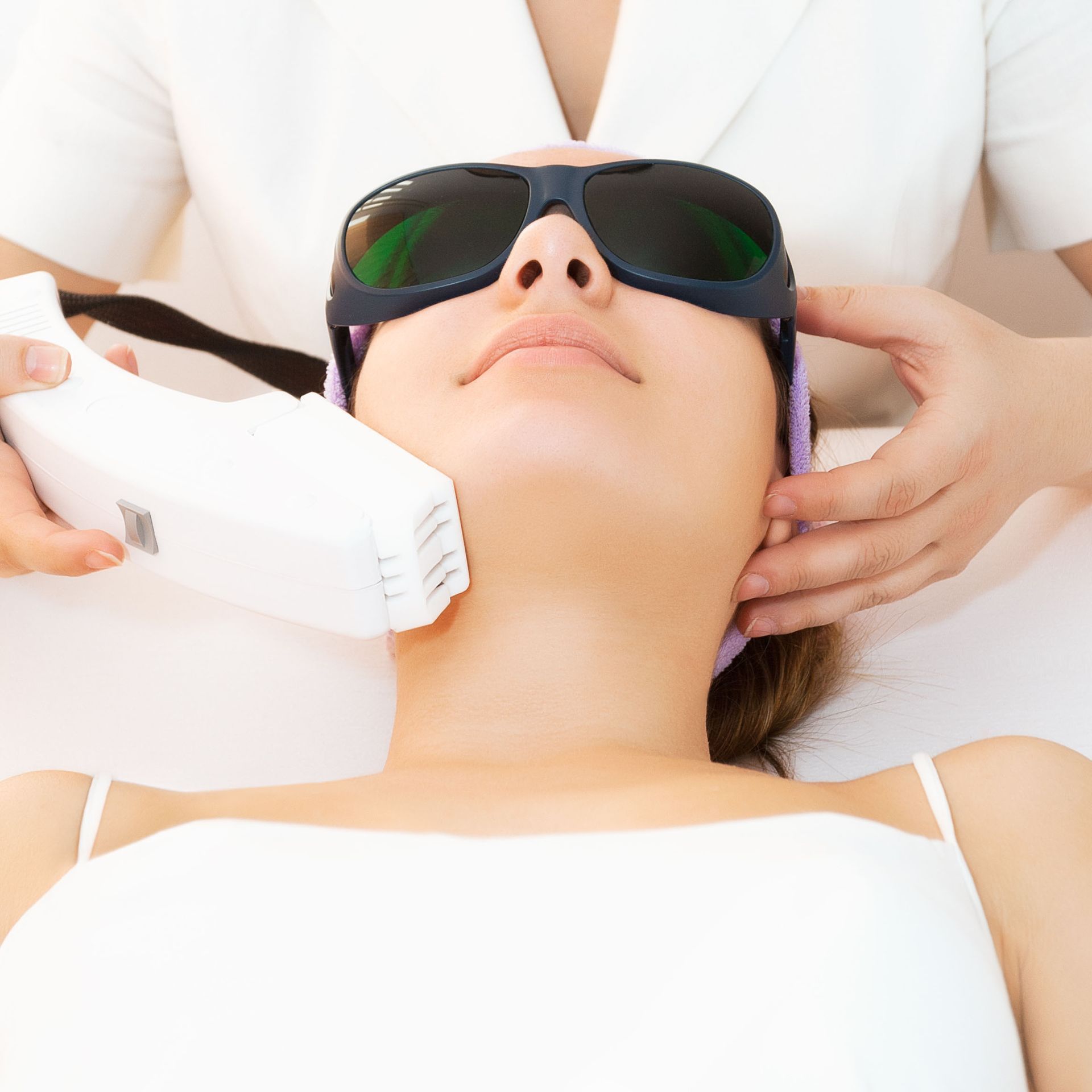 Woman receiving laser hair removal on her neck; wearing safety glasses. A technician holds the laser device.