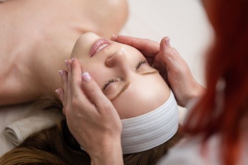 A woman receiving a facial massage, eyes closed, lying on a table.  Hands gently cradle her face.