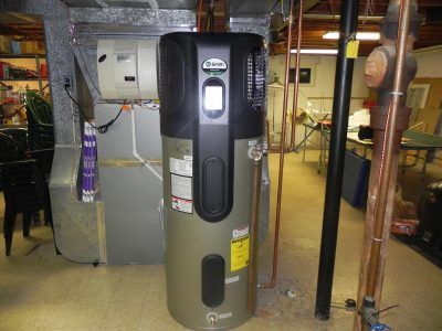Tall water heater in a basement utility room with exposed pipes and equipment.