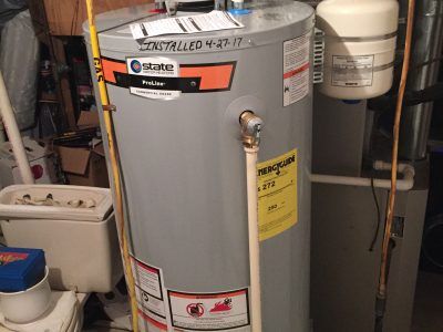 Gray Rheem water heater in a utility room with pipes and nearby equipment.