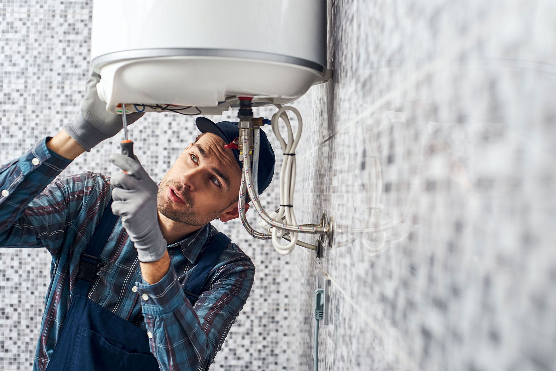 Plumber repairing a water heater with tools in a tiled utility room