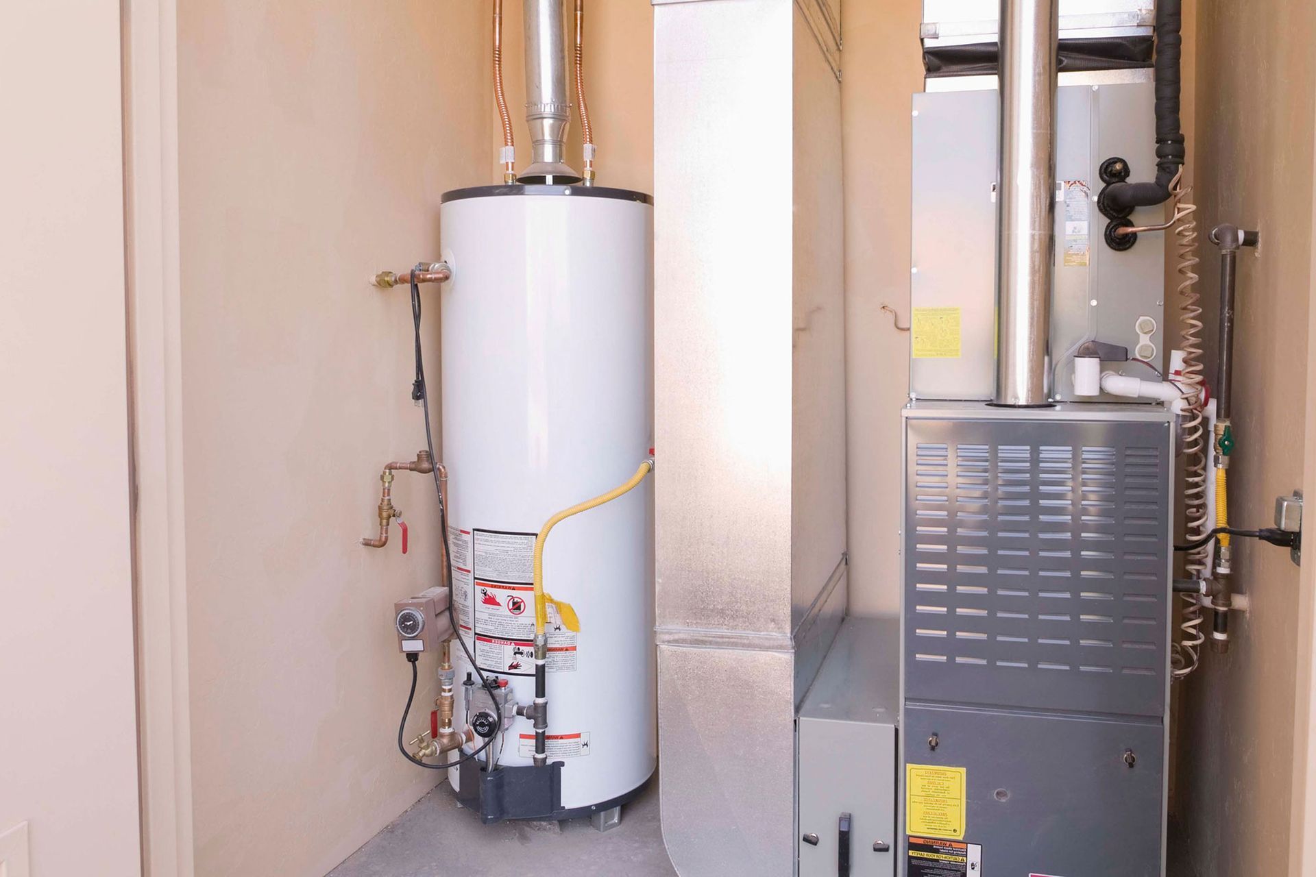 Water heater and furnace in a narrow utility closet with exposed pipes.