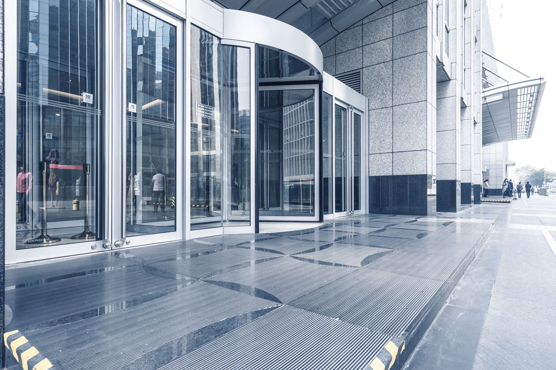 A modern office building entrance with revolving glass doors and a shiny, tiled ground.