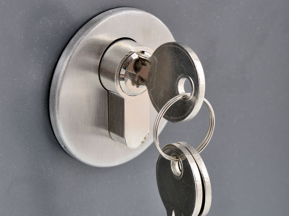 Key in a silver lock on a gray surface, with two keys on a ring.