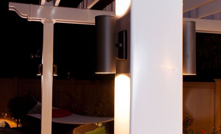 White pergola with dark cylindrical lights, illuminating a nighttime outdoor space.