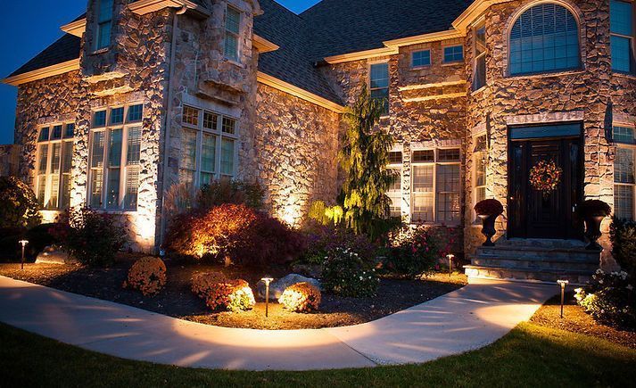 Night view of a stone house lit up with landscape lighting along a pathway and highlighting the facade and landscaping.
