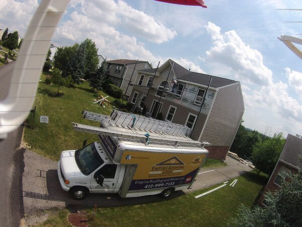 A roofing company truck is parked in front of a house