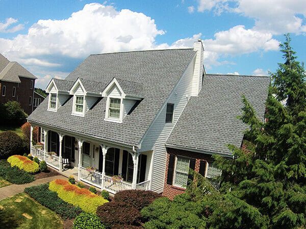 An aerial view of a large house with a gray roof and a large porch.