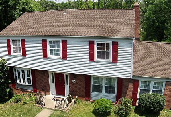 An aerial view of a white house with red shutters and a brown roof.